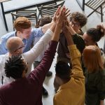 A diverse group of professionals high-fiving in a modern office, showcasing teamwork and collaboration.